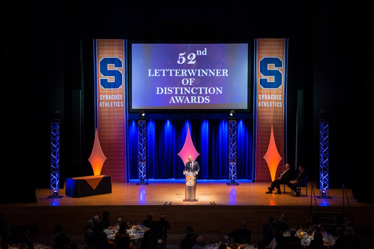 Stage set for an awards ceremony with a speaker at the podium. Blue and orange lighting.