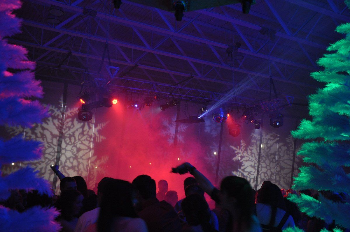 People dancing at a party with stage lights, red fog, and snowflake projections on the wall.