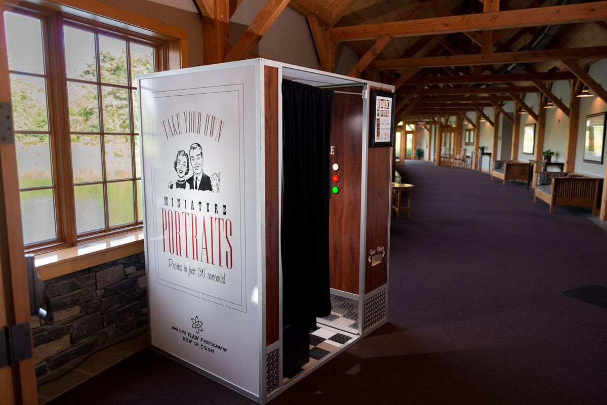 Photo booth in a hall with wooden beams. Booth is white with black curtain entrance.