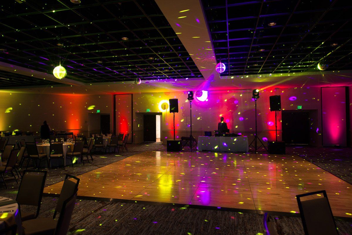 A dance floor with a DJ, disco balls, and colorful lighting in a venue.