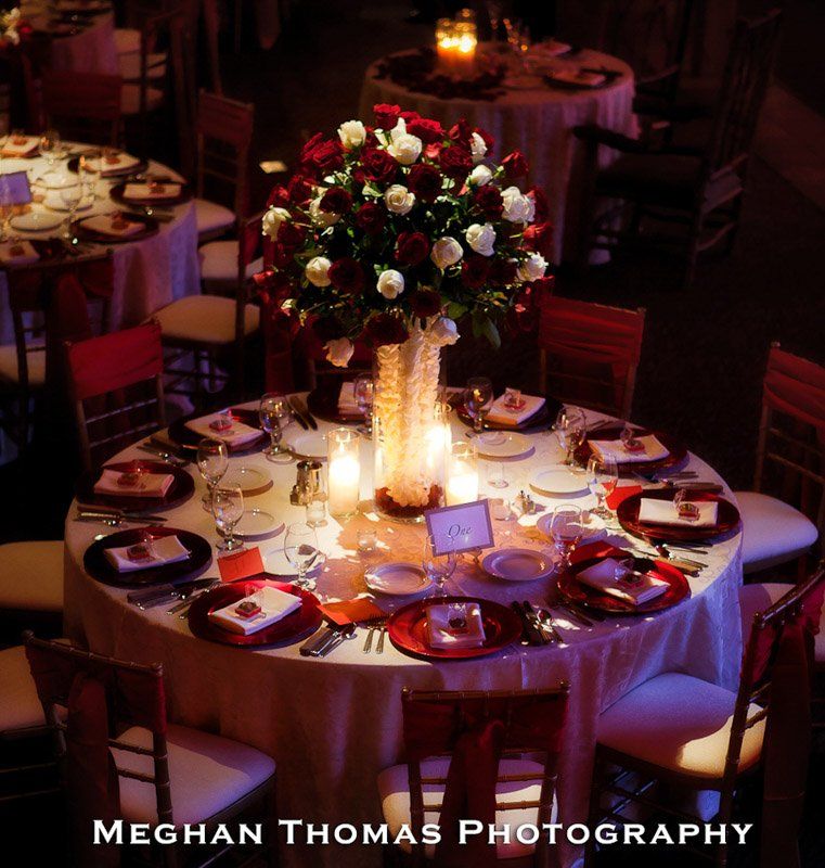 Round table set for a formal event, red and white floral centerpiece, lit candles.