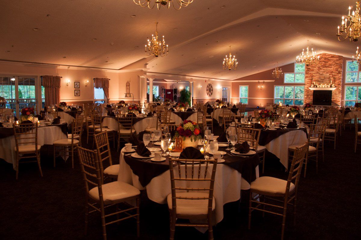Elegant ballroom with round tables set for an event, gold chairs, dark tablecloths, and chandeliers.