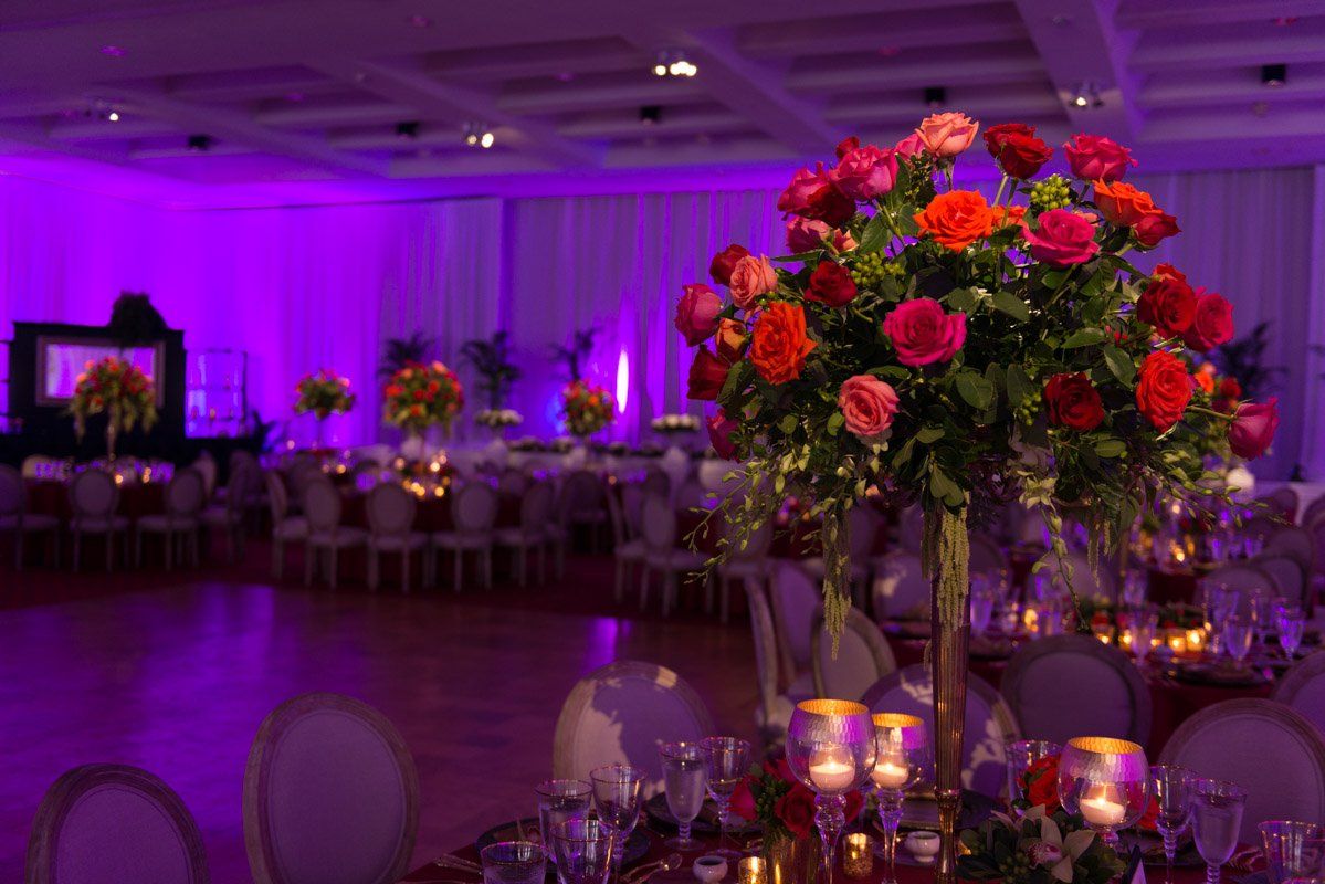 Elegant wedding reception with purple lighting, floral centerpieces, and set tables.