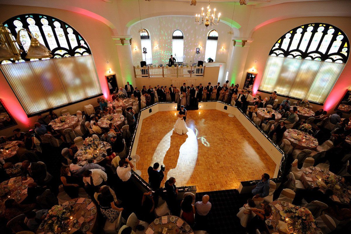 Wedding reception in a grand ballroom with dancing couple on the floor. Guests seated at tables.
