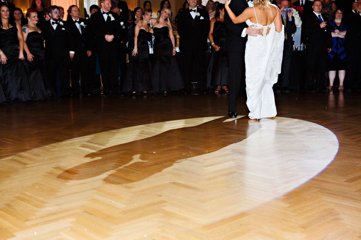 Couple dancing under a spotlight on a wooden dance floor at a formal event.