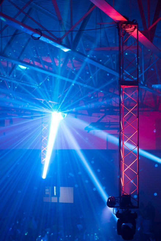 Blue and red stage lighting illuminating a large venue, with a central beam and a truss.