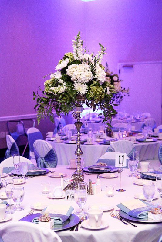 Elegant floral centerpiece on a round table set for a wedding reception, with blue and white accents.