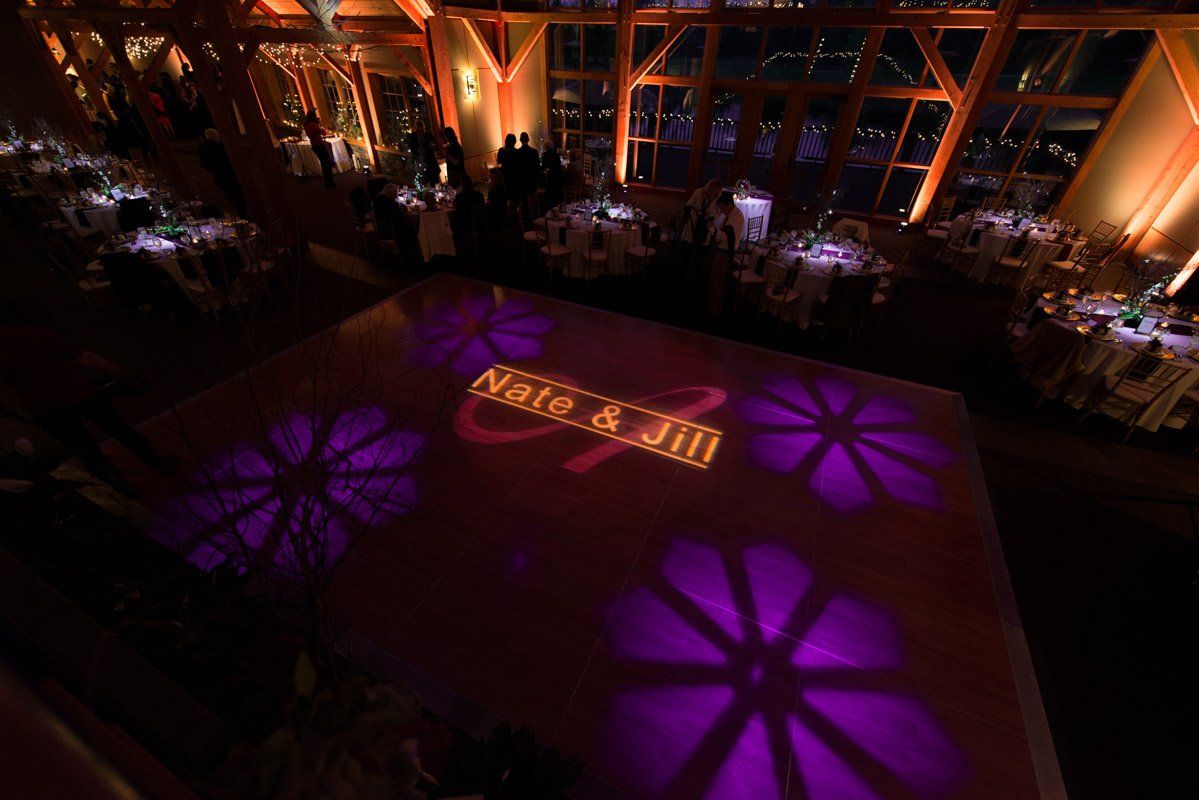 Dance floor at a wedding with purple flower lights and the couple's names, Nate & Jill, lit up.