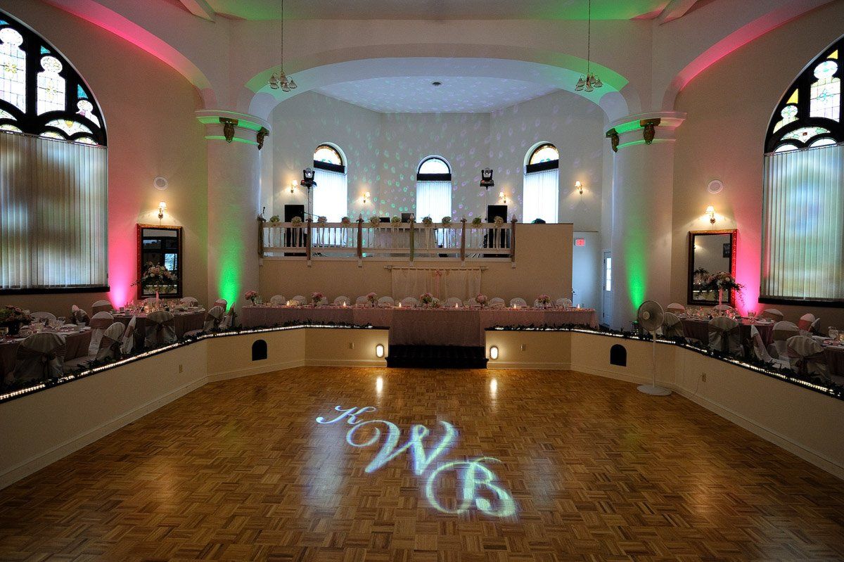 Ballroom with wooden dance floor, stage, tables, and colorful lighting. 