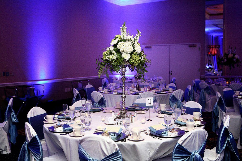 Formal dining room with round tables set for a celebration. Blue and white color scheme, large floral centerpieces.