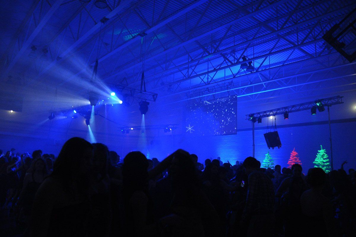 Blue-lit crowd at a concert. Stage with lights and decorations, silhouettes of people, dark ambiance.