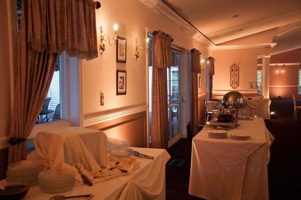 Buffet tables in a warmly lit restaurant hallway. Beige linens, food, and decorative curtains are visible.