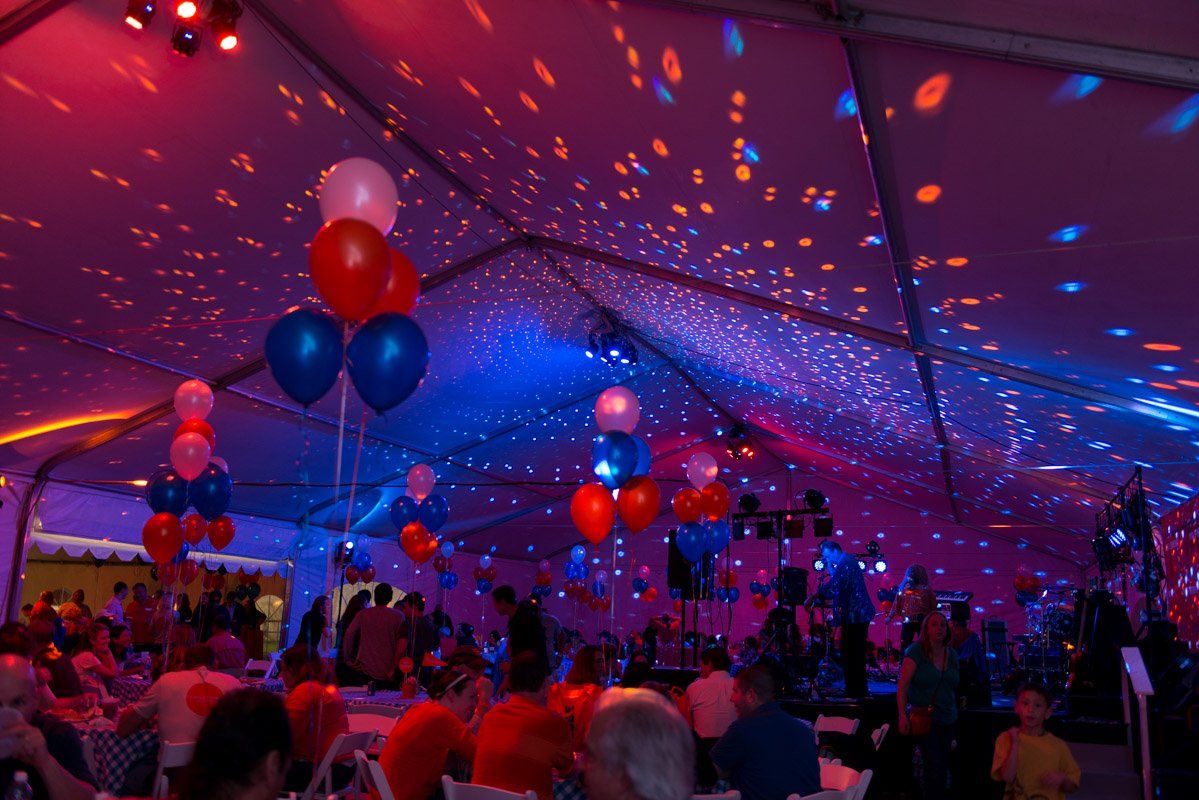 Party tent lit with red and blue lights. Balloons and people are visible.