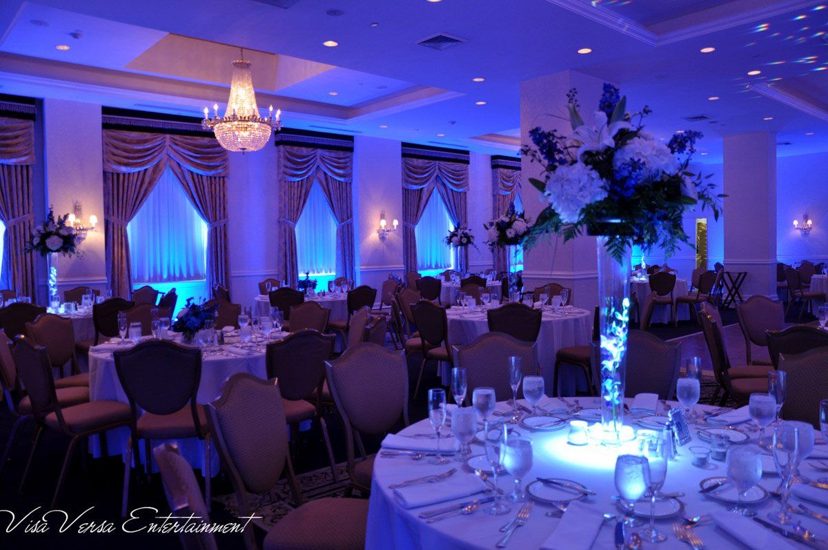 A banquet hall set for an event. Blue lighting illuminates tables, flower arrangements, and curtains.