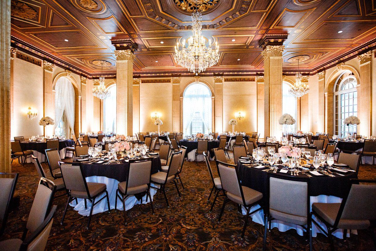 Elegant ballroom set for an event, featuring round tables with centerpieces, chandeliers, and ornate ceiling.