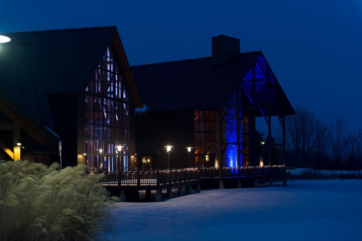 Building with glass walls and blue uplighting at night, reflecting in snow.