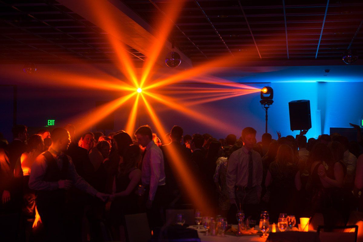 People dancing under orange stage lights in a dark room; blue light on walls.