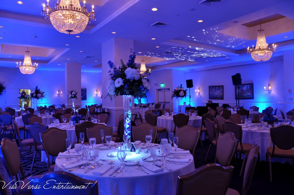 Wedding reception hall with tables set for guests under blue up lighting.