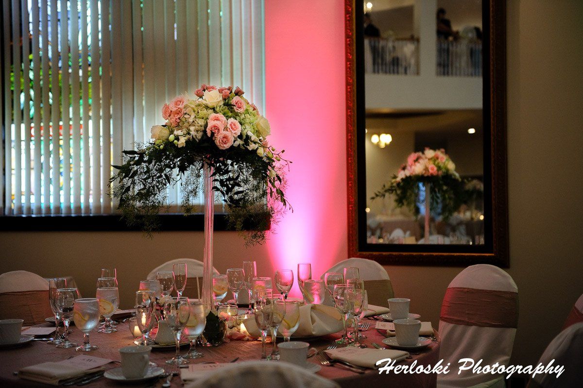 Elegant wedding table setting with floral centerpiece, pink uplighting, and mirror reflection.