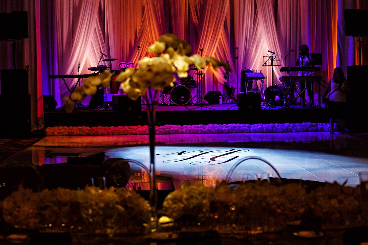 Stage with a band set up, soft lighting, floral centerpiece in foreground, mirrored floor.