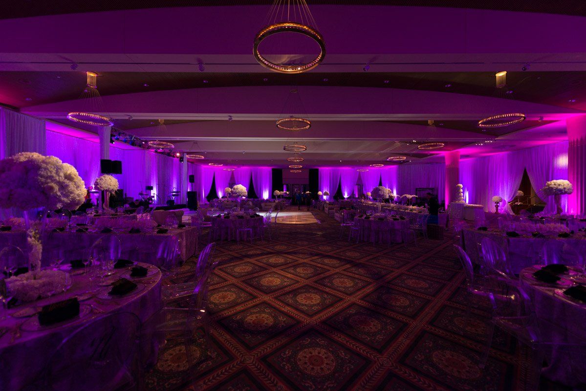 Reception hall with purple lighting, decorated tables, and floral arrangements.
