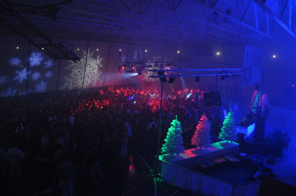 Concert with a crowd, stage with DJ and Christmas trees, blue and red lighting, snowflakes projected on the wall.