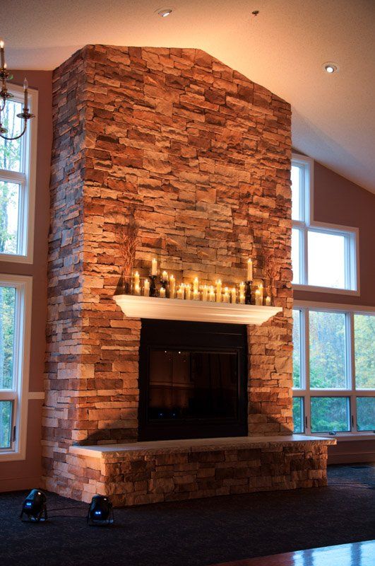 Brick fireplace with candles on the mantel, flanked by large windows in a spacious room.