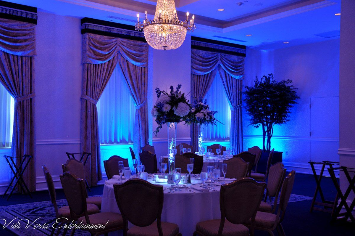 Formal dining room with round table, lit with blue lights, floral centerpiece, chandelier, and elegant drapes.