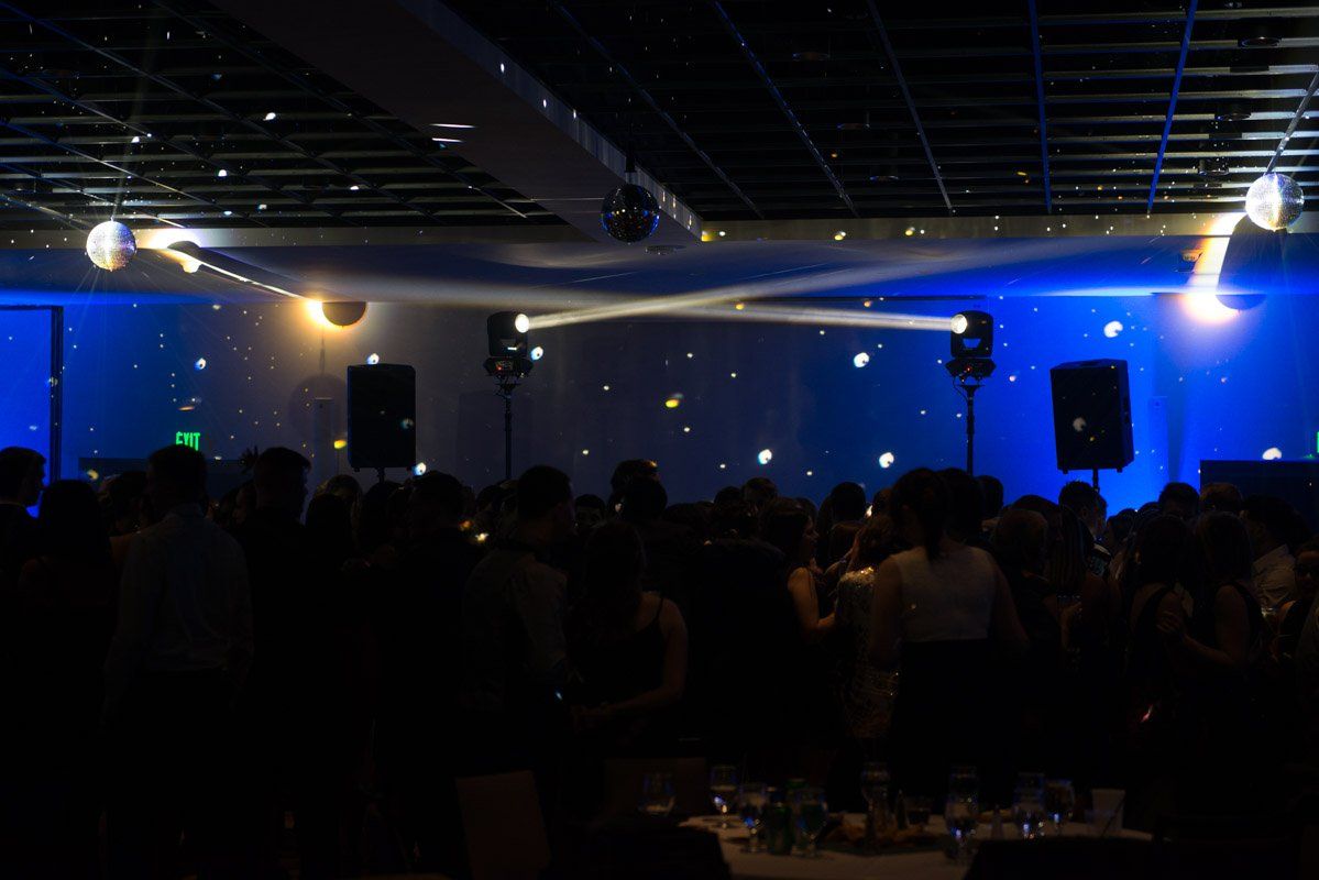 A brightly lit dance party with disco balls, spotlights, and a crowded dance floor with people.
