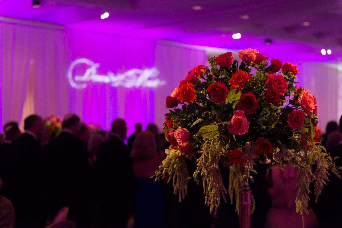 Red and pink floral arrangement at an event with purple lighting; people in the background.