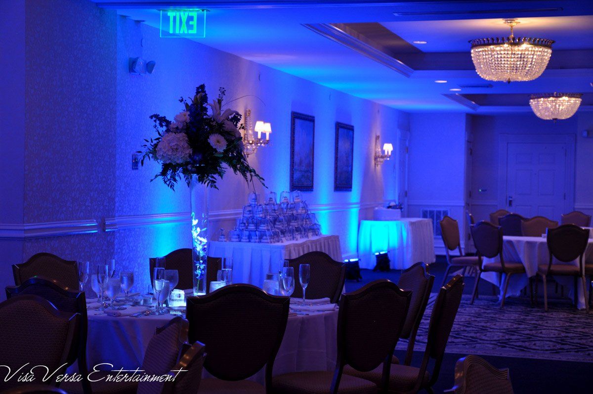 A banquet hall with blue up-lighting, tables, flowers, and chandeliers.
