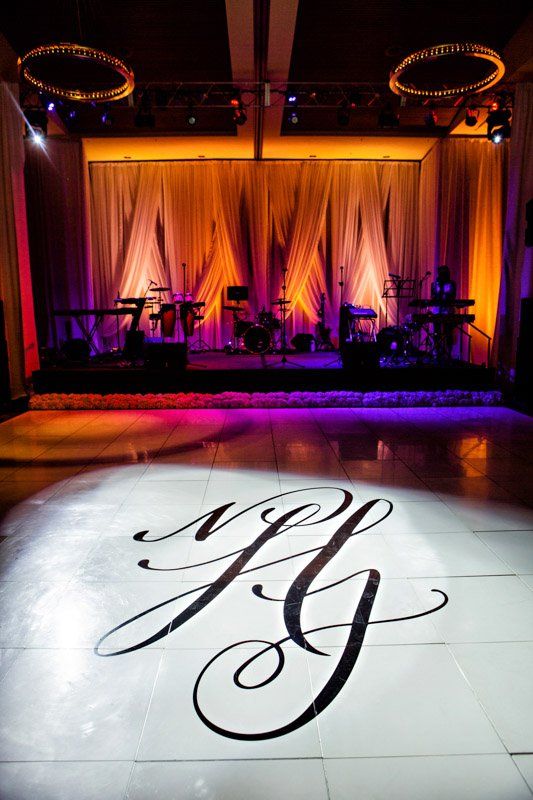White dance floor with black monogram, band stage in background with orange and purple lighting.