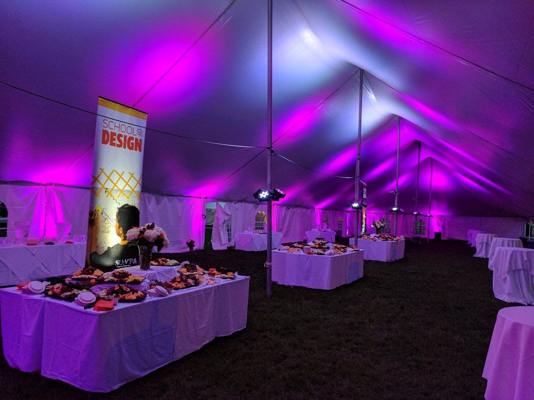 Inside tent, tables set with food, bathed in purple lighting. Event banner, white tablecloths.
