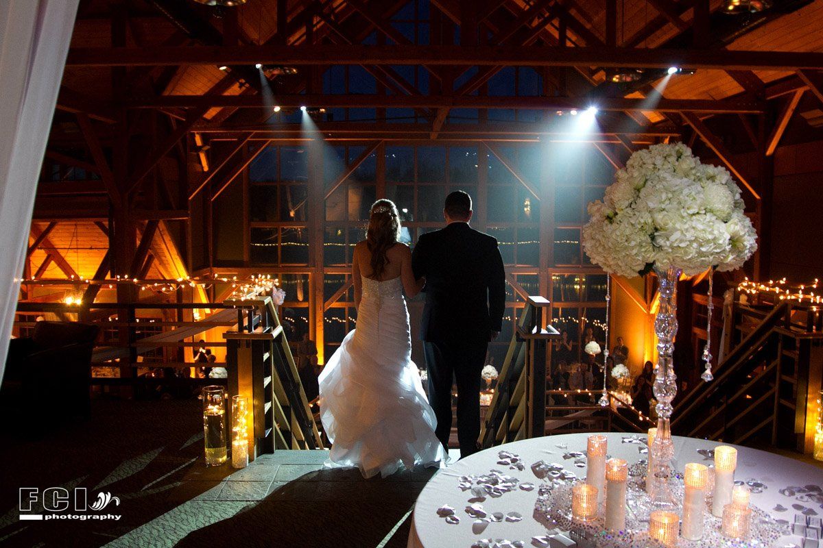 Bride and groom walk away from the camera in a candlelit barn.
