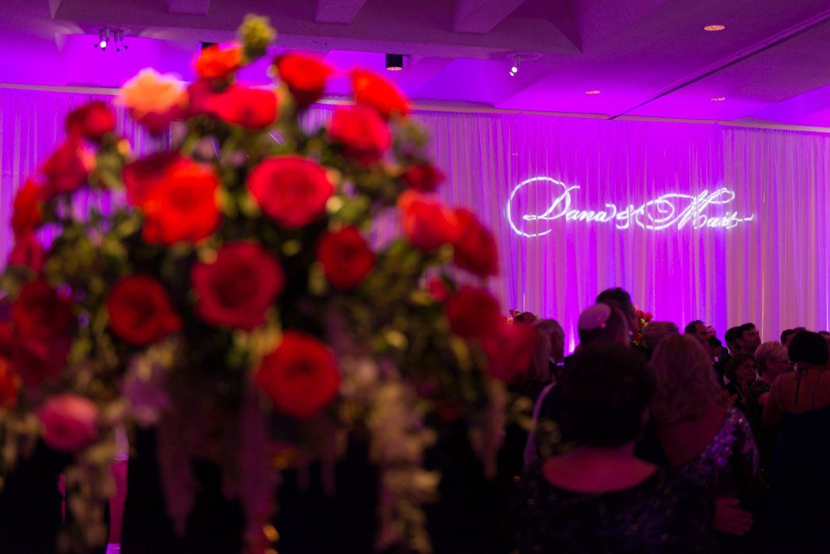 Red flowers in foreground; event with purple lighting; sign reading 