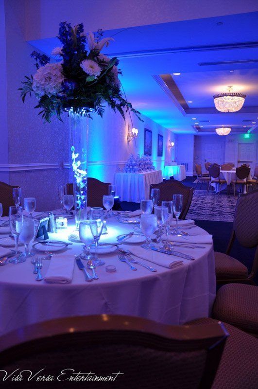 Round table set for a formal event, blue lighting, tall floral centerpiece in a glass vase.
