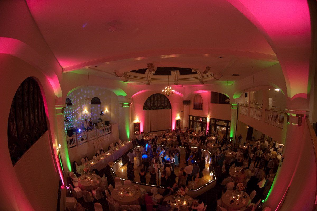 Large ballroom with people dancing under pink and green lights.