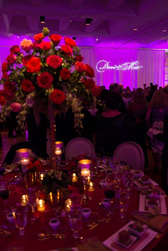 Elegant event: table set with red flowers, candles, and place settings. Purple uplighting.