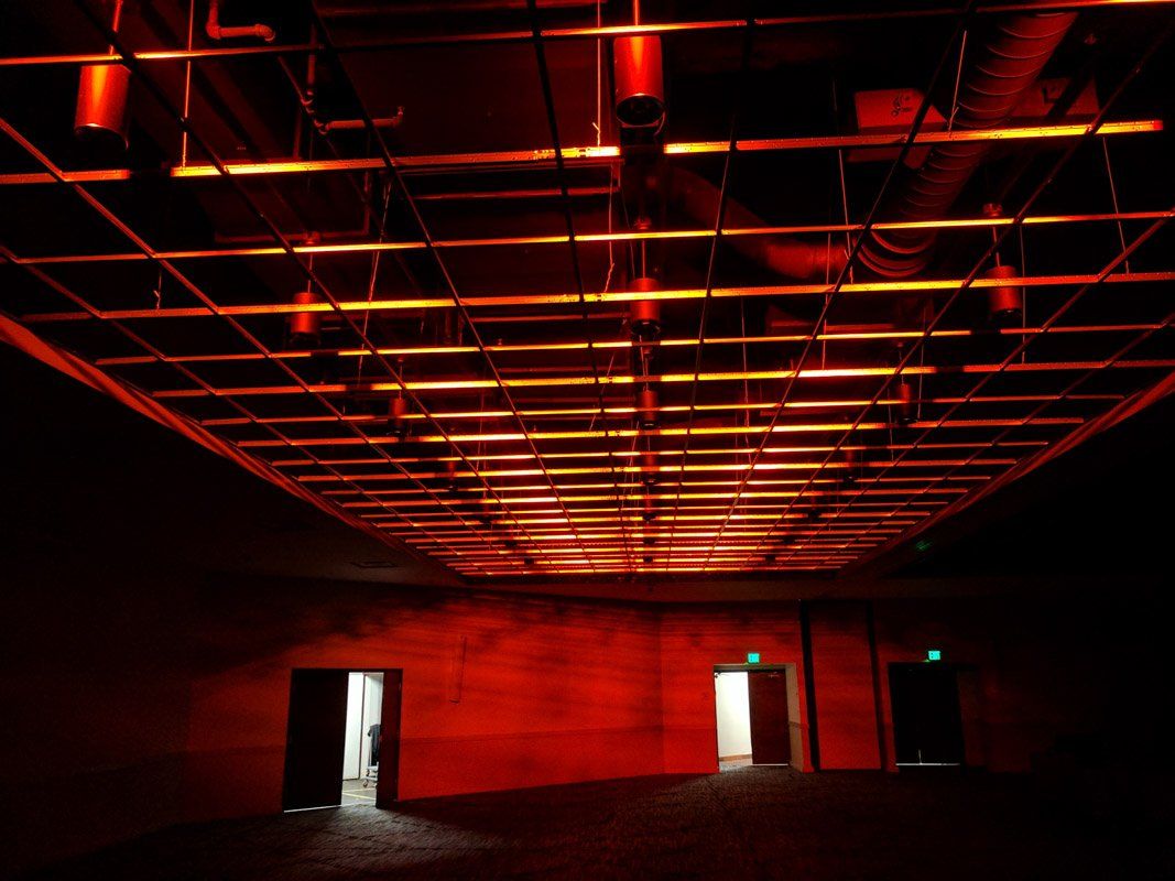 A dark room with red lighting. Doors and a grid ceiling are visible.