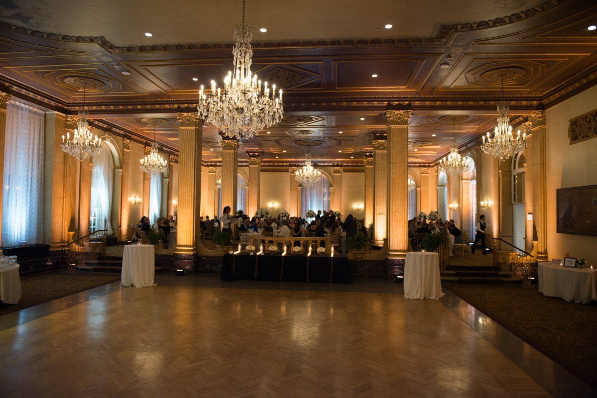 Ornate ballroom with chandeliers, columns, and tables set for an event.