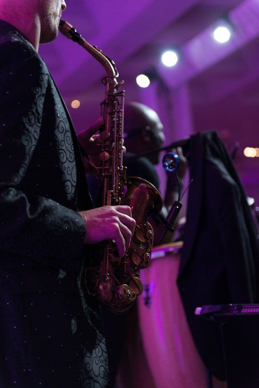 Saxophonist in black jacket playing saxophone with purple stage lights.