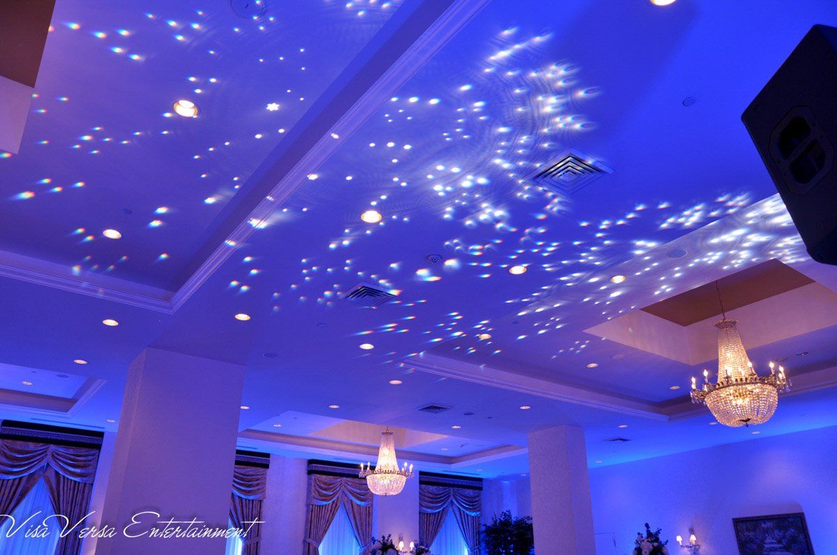 Blue-lit event space ceiling with star-like light projections, chandeliers, and pillars.
