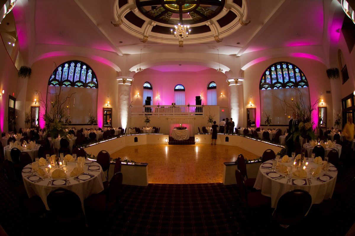 Elegant ballroom set for an event, with round tables, a dance floor, and pink uplighting.