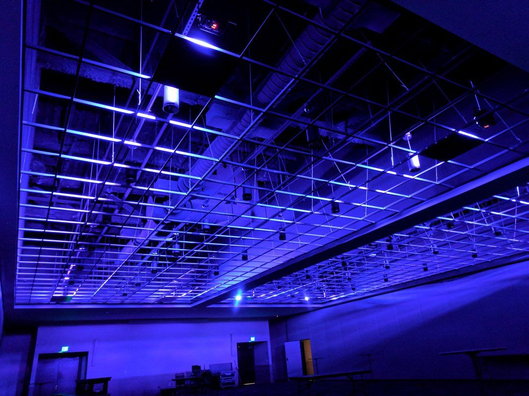 Blue-lit, high-ceilinged room with a metal grid overhead. Doors visible along the far wall.