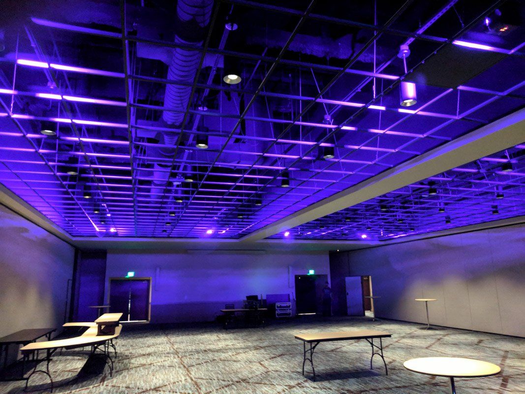 Empty room with tables, doors, and a grid ceiling illuminated in purple.