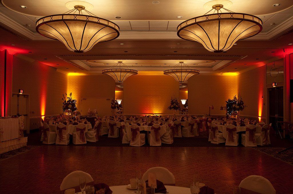 Wedding reception hall with tables set and amber uplighting.