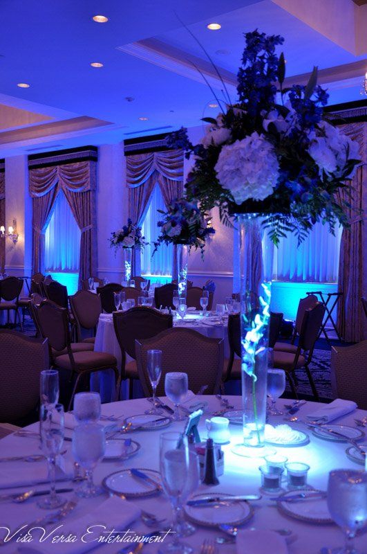 Elegant banquet hall with blue uplighting, decorated tables, and floral centerpieces.