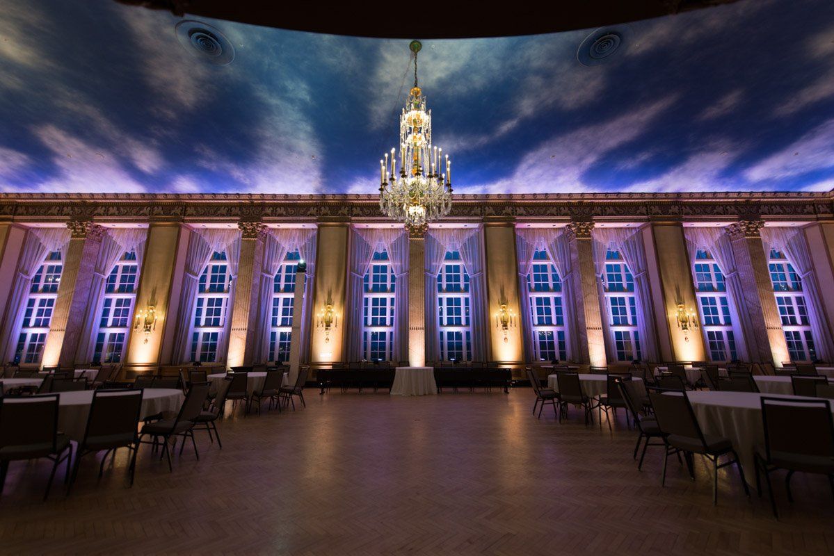 Grand ballroom with a cloud-painted ceiling, chandelier, columns, and tables.