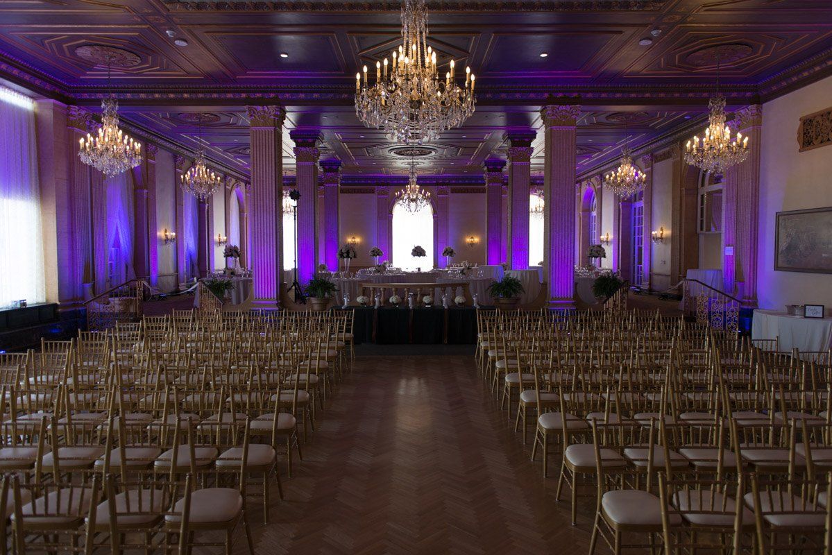 Elegant ballroom set for an event with gold chairs, purple lighting, and chandeliers.