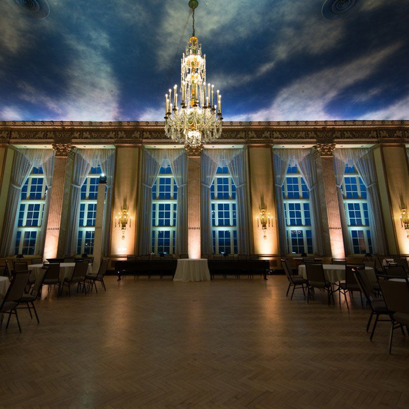 Ornate ballroom with a large chandelier, high windows, and a painted sky ceiling.